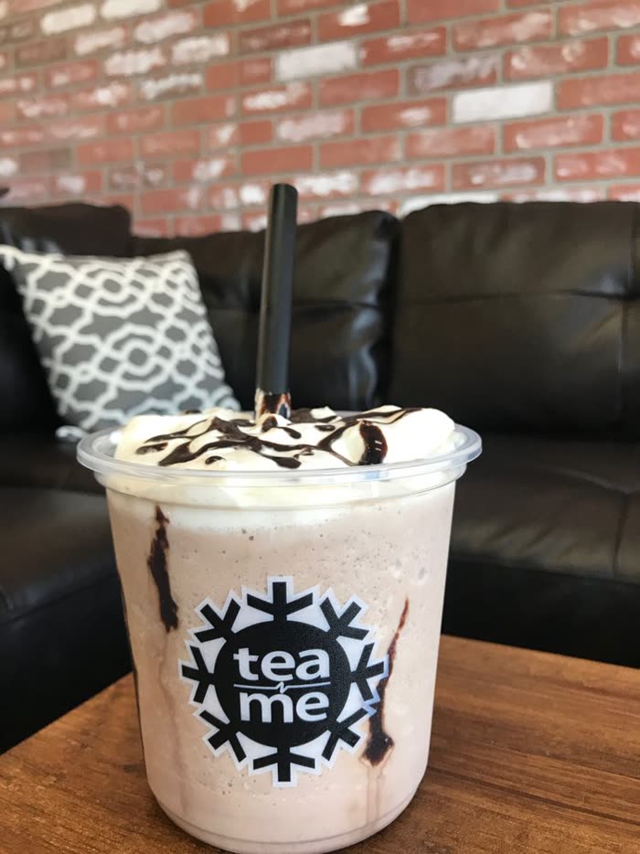 A blended drink with whipped cream and chocolate drizzle on the table by the couch