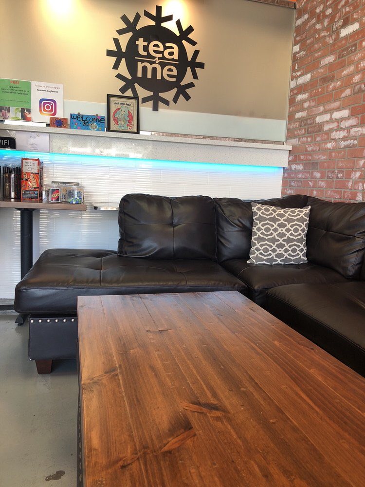 A black leather couch and a long wooden table under the Tea N' Me snowflake painted on the wall.