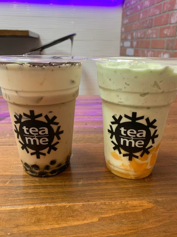 Two drinks with boba on a wood table in front of the brick wall