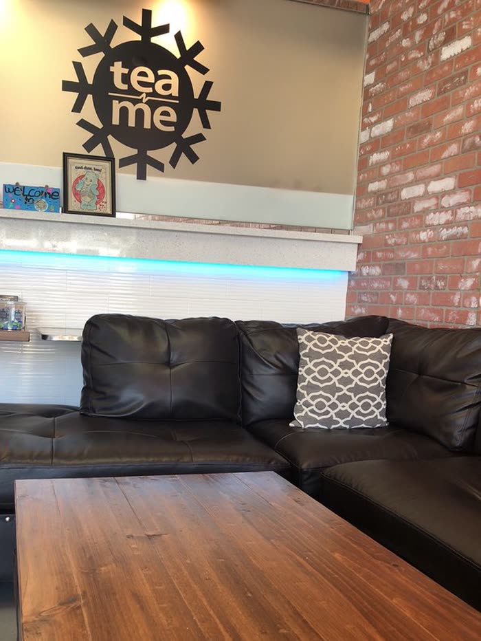 The black leather sectional and the long wood table under the tea n' me wall mark