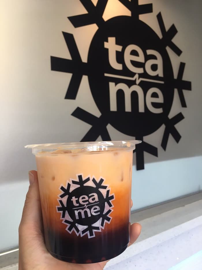 A layered orange iced tea with boba held up in front of the tea n' me wall mark